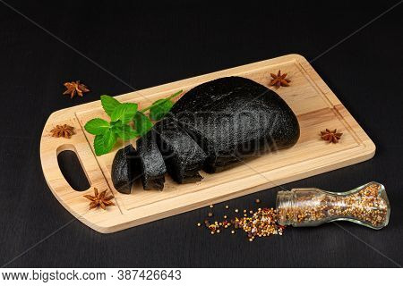Fresh Black Rye Bread On A Cutting Board With Seasonings Sprinkled On A Black Wooden Table