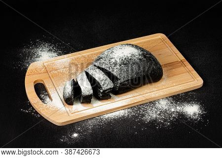 Fresh Black Rye Bread On A Cutting Board With Flour On A Black Wooden Table