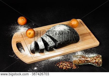 Fresh Black Rye Bread On A Cutting Board With Seasonings Sprinkled With Flour On A Black Wooden Tabl