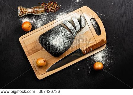 Fresh Black Rye Bread On A Cutting Board With Seasonings Sprinkled With Flour On A Black Wooden Tabl