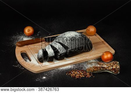 Fresh Black Rye Bread On A Cutting Board With Seasonings Sprinkled With Flour On A Black Wooden Tabl