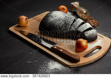 Fresh Black Rye Bread On A Cutting Board With Seasonings Sprinkled With Flour On A Black Wooden Tabl
