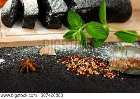 Fresh Black Rye Bread On A Cutting Board With Seasonings Sprinkled With Flour On A Black Wooden Tabl