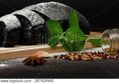 Fresh Black Rye Bread On A Cutting Board With Seasonings Sprinkled With Flour On A Black Wooden Tabl