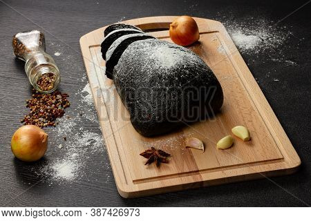 Fresh Black Rye Bread On A Cutting Board With Seasonings Sprinkled With Flour On A Black Wooden Tabl