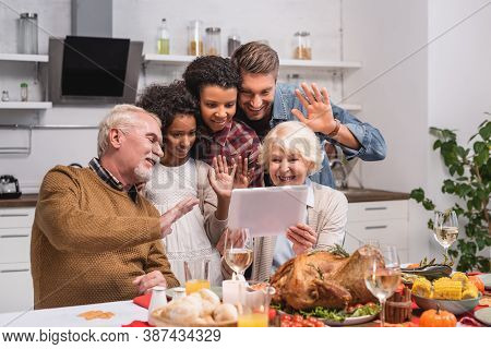Focus Of Multicultural Family Waving At Digital Tablet During Video Call And Thanksgiving Celebratio