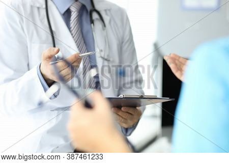 Doctor With Phonendoscope Holds Pen And Folder With Documents In Closeup Conversation With Another D