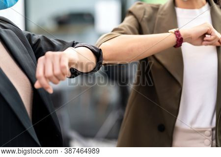 Close up two businesswomen do alternative greeting in new normal office lifestyle. They wear protective face mask and use elbow touch instead of hand shake to reduce infection of coronavirus COVID-19.