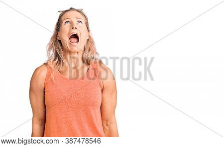 Middle age fit blonde woman wearing casual summer clothes and sunglasses angry and mad screaming frustrated and furious, shouting with anger. rage and aggressive concept. 