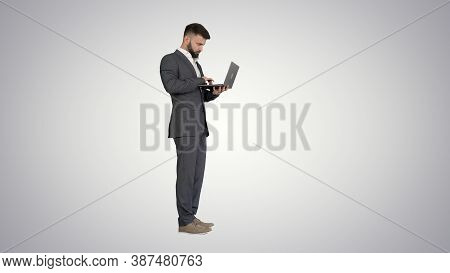 Handsome Businessman Standing And Working On Laptop On Gradient