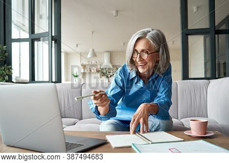 Happy Mature Older Woman Video Calling On Laptop Working From Home. Smiling 60s Middle Aged Business