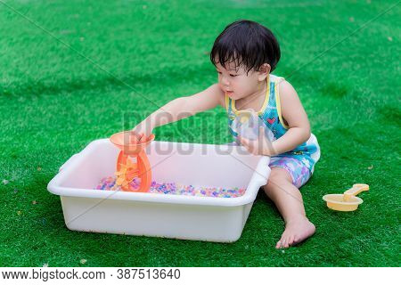 2 Year Old Child Boy Is Playing Colorful Water Beads In White Basin. Kid Picks Up Rainbow Beads On O