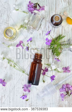 Top View On Bottles Of Essentiel Oil Spilled Among Little Pink Flowers On A Table