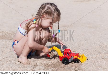Joyful Three-year-old Girl Plays With A Machine In The Sand On The Beach