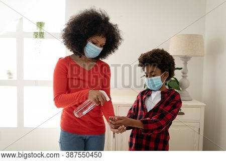 Mixed race mother with son enjoying family time together at home, social distancing and self isolation in quarantine lockdown, wearing face masks, disinfecting their hands