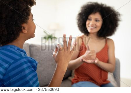 Mixed race mother with son enjoying family time together at home, social distancing and self isolation in quarantine lockdown, sitting on a couch, playing rock, paper, scisors