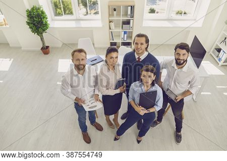 Group Of Smiling Business People Standing With Documents And Looking At Camera Ahead