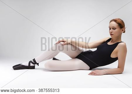 Relaxing Caucasian Professional Ballet Dancer In Body Suit  And Pointes Shoes Posing Against White