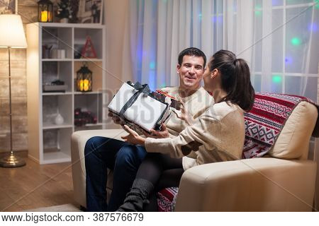 Young Wife Giving Her Husband A Big Present On Christmas Day. Happy Couple.