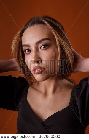 Charming Elegant Fashion Model Wearing Black Dress With Deep Neckline Posing On Orange Background. A