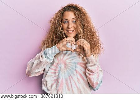 Beautiful caucasian teenager girl wearing casual tie dye sweatshirt smiling in love showing heart symbol and shape with hands. romantic concept. 