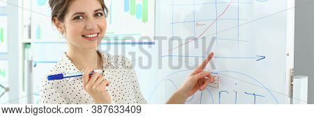 Portrait Of Smart Lady Pointing At Important Business Charts And Graphs On High-tech Glass Board. At