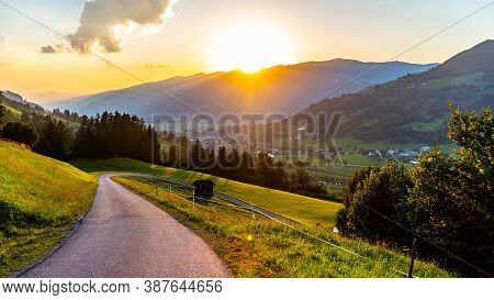 Romantic Sunset In The Mountains. Alpine Rural Curvy Road, Green Meadows And High Peaks Of Austrian 