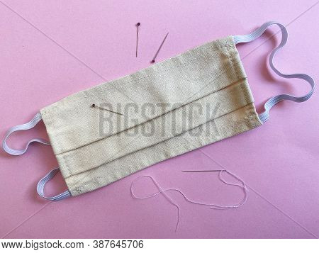 White Homemade Facemask With Needle, Thread And Pins On Pink Backround