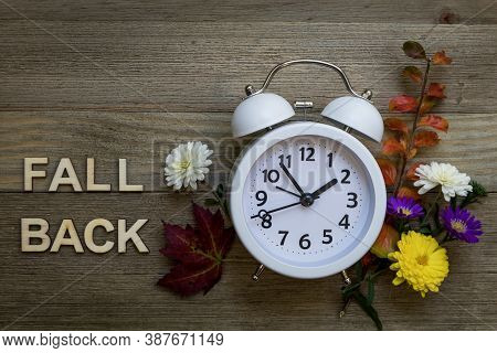Fall Back Daylight Saving Time Concept With White Alarm Clock And Fresh Fall Flowers Foliage On Hand