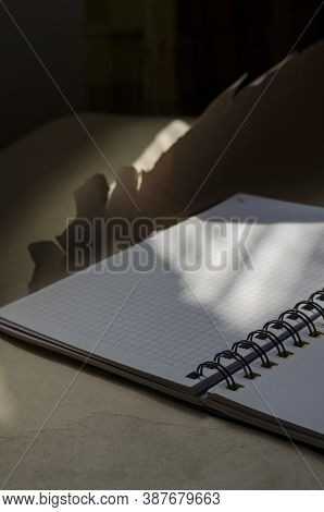 Open Spring-bound Notebook In Sunlight. New Diary With Blank Pages On Torn Wrapping Paper. Side View