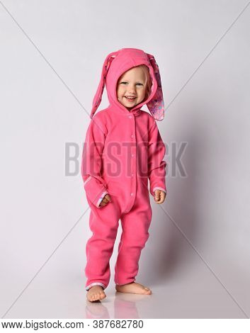 Laughing Barefooted Cute Blonde Baby Girl In Pink Warm Comfortable Jumpsuit Stands Looking At Camera