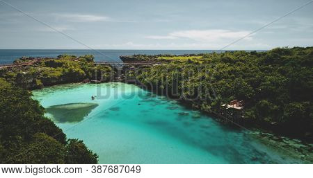 Turquoise lake with resting people aerial view. Tourists swimming at azure crystal clean lagoon admist green tropic trees landscape. Cinematic summer vacation at salt water Weekuri loch in drone shot