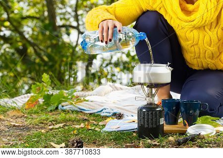 Young Beautiful Girl In A Yellow Sweater Makes Coffee In The Forest On A Gas Burner. Making Coffee O