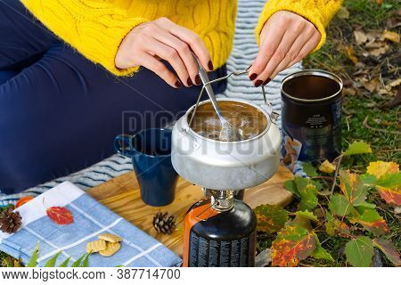 Young Beautiful Girl In A Yellow Sweater Makes Coffee In The Forest On A Gas Burner. Making Coffee O