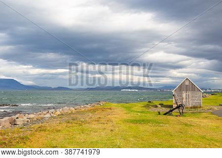 Sculpture Anchor And Shore Walk, Seltjarnarnes, Faxafloi Bay, Reykjavik, Iceland. Town In The Backgr