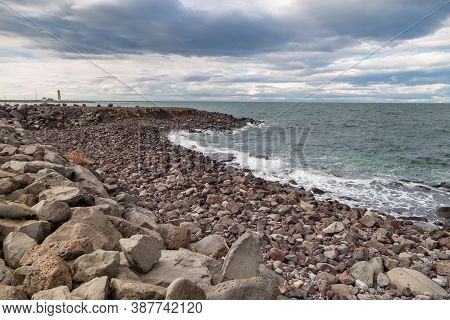 Rocky Coast Of Faxafloi Bay, Lighthouse In The Background. Seltjarnarnes, Reykjavik, Iceland.