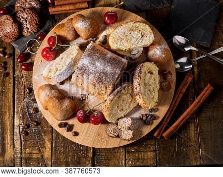 Sand nut chocolate cookies and rolled biscuit on board and cinnamon stick and straw pastry on kitchen on wood table in rustic style top view. Cups of tea and dessert spoon. Top view.