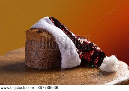 Panettone With Chocolate Chips And Santa Claus Hat On Rustic Wood With Gradient Background In Red An