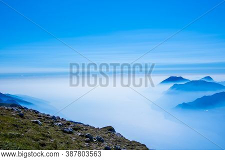 The Peaks Of The Alps Around Lake Garda Surrounded By Fog With Blue Sky Seen From Monte Altissimo, T