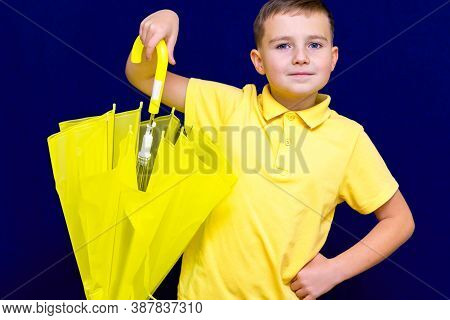 Attractive Surprised Caucasian Blond Schoolboy Holds Unexpanded Umbrella On Blue Studio Background.b