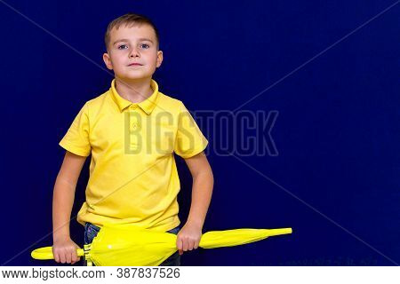 Attractive Surprised Caucasian Blond Schoolboy Holds Unexpanded Umbrella On Blue Studio Background.b