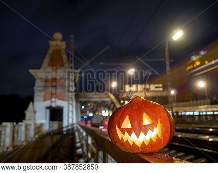 Halloween Pumpkin With A Glowing Grimace At Night On The Railway Bridge. In The Background There Are