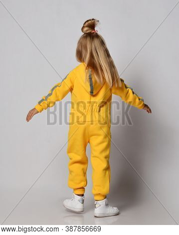 Full-growth Portrait Of Blonde Kid Girl With Stylish Hairstyle Wearing Modern Yellow Jumpsuit And Sn