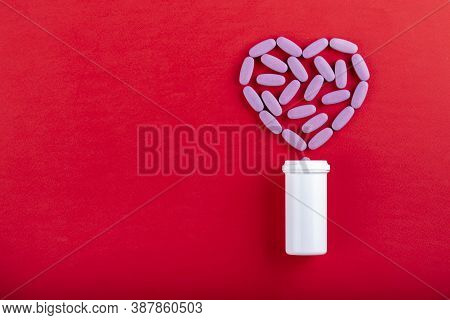 Tablets And Bottle On Red Background Top View. The Tablets Are Laid Out In The Shape Of A Heart. Med