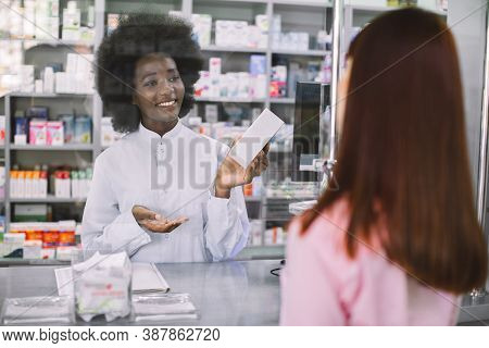Pharmacy, People And Healthcare Concept. Smiling Female Afrcian Pharmacist Giving Medicine To Young 