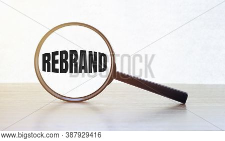 Magnifying Glass With Text Rebrand On Wooden Table.