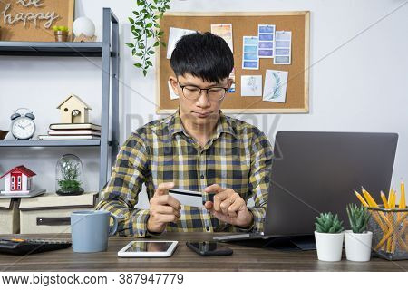 Asian Man Holding Credit Card And Typing Information On Internet With Laptop At Home, Online Shoppin