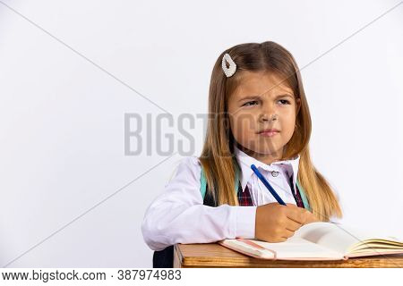 Stressed Little Girl In School Uniform Sitting At Desk Isolated, White Background. Schoolgirl Unhapp