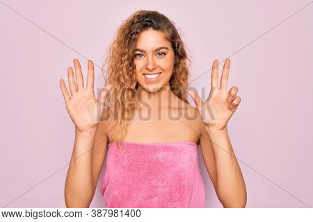 Beautiful blonde woman with blue eyes wearing towel shower after bath over pink background showing and pointing up with fingers number eight while smiling confident and happy.