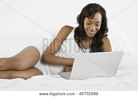 Uśmiechnięte młode African American kobieta korzysta z laptopa w łóżku